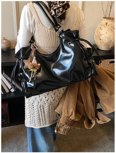 Détail d'un sac à bandoulière noir brillant avec cordon latéral et charm en peluche