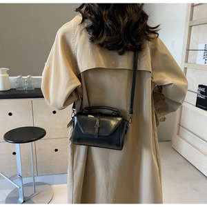 Detail view of a black glossy leather crossbody bag with metal buckle and shoulder strap
