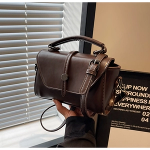Detail view of a vintage dark brown handbag featuring a round metal clasp and top handle