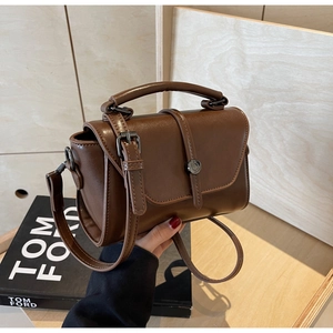 Detail of a vintage dark brown leather handbag featuring smooth texture and metal magnetic buckle