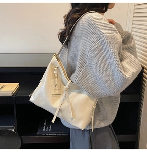 Model wearing a large cream shoulder bag with soft leather texture and slender straps