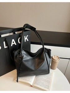 Detailed view of black soft leather tote bag with unique knotted strap and side snap buttons