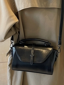 Classic black leather handbag with metal buckle worn by model in a stylish trench coat