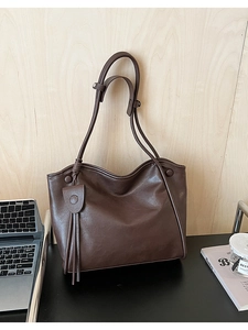 Macro shot of large dark brown leather tote bag with stylish tassel on office desk