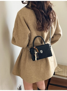 Detail of black crossbody bag with vintage metal clasp and beaded tassel on a wool coat