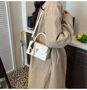 Detail of cream crossbody bag with beads on a khaki trench coat for trendy ladies