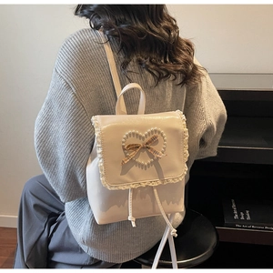 Détail d'un sac à dos beige avec un cœur en perles et des finitions en dentelle blanche
