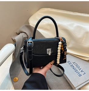 Detail of black leather handbag with silver twist lock and decorative wooden bead charm