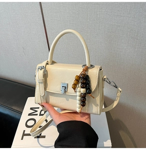 Top view of cream white PU leather crossbody bag with wooden bead charm on a gift box