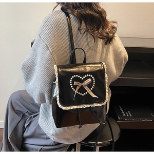 Détail du sac à dos en cuir noir avec bordure en dentelle et cœur en perles sur pull gris