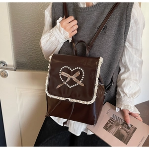 Détail d'un sac à dos en cuir marron café avec bordure en dentelle et nœud en perles