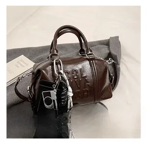 Detail of dark brown Boston bag featuring embossed letters and decorative camera charm