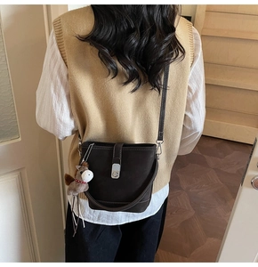 Detail of dark brown bucket bag with silver twist lock and horse charm on long strap