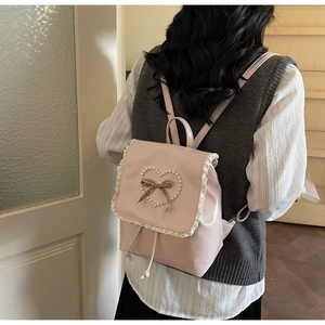Detail of light pink backpack featuring white lace trim and a pearl heart with checkered bow