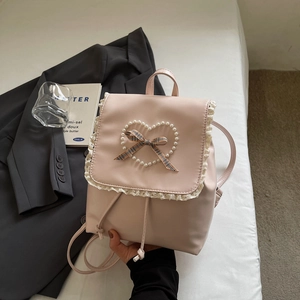Détail du sac à dos en cuir rose avec bordure en dentelle blanche et nœud en perles