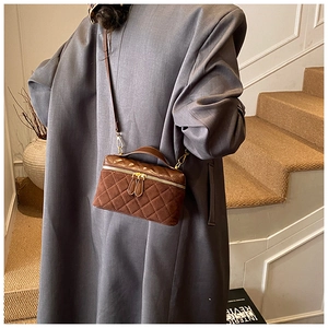 Detail shot of brown quilted suede crossbody bag featuring gold zippers and leather top handle