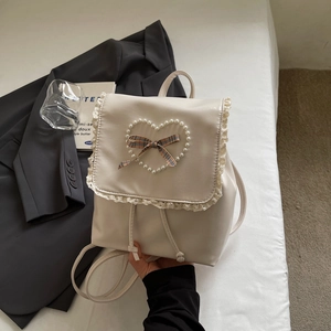 Détail d'un sac à dos crème avec cœur en perles, nœud à carreaux et bordure en dentelle
