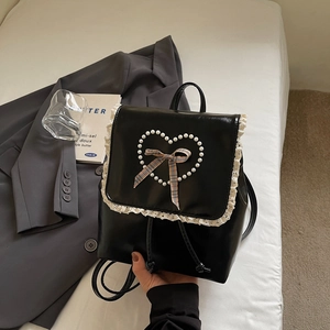 Détail du sac à dos en similicuir noir avec dentelle blanche, cœur perlé et nœud