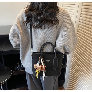 Détail d'un cabas noir mat avec breloque ours brodée et logo de la marque sur le sac