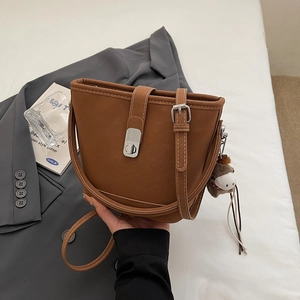 Detail of a brown leather bucket bag featuring white stitching and a horse bag charm