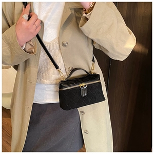 Close-up of black quilted vanity case bag with gold hardware and chain strap on model