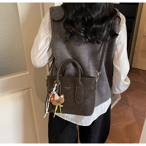 Détail du sac en cuir mat marron foncé avec logo doré, breloque ours et écharpe