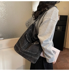 Dettaglio di una borsa tote in denim nero lavato con cuciture a contrasto e tasche cargo