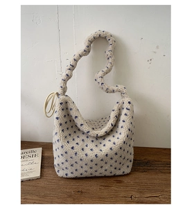 Detail of beige fleece tote bag with blue dots and wavy pleated handle on wood
