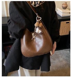Close-up of brown hobo bag with heart charm and leopard bow on model in black suit