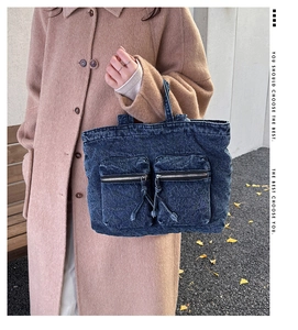 Close-up of a blue denim tote bag with dual front zipper pockets and utility drawstrings