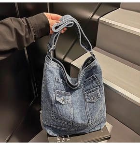Dettaglio della grande borsa tote in denim blu con due tasche frontali e fibbie metalliche
