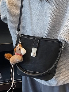 Minimalist black bucket crossbody bag with white stitching and plush charm on grey sweater