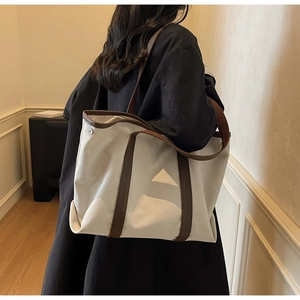 Détail du grand sac cabas en toile crème avec anses en cuir marron et boucles argent