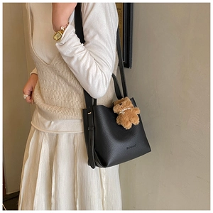 Detail of black lychee grain bucket bag with a brown plush bear charm and brand logo