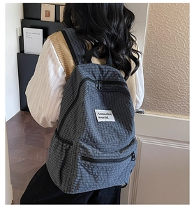 Detailed view of grey plaid pattern canvas backpack with brand label on front pocket