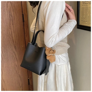Detail of black lychee grain leather bucket bag with cute brown bear plush charm