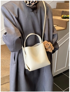Detail of cream bucket bag with lychee texture featuring a cute brown plush bear charm