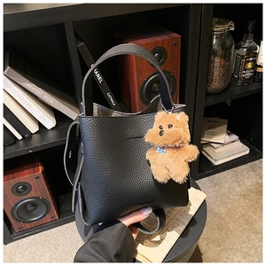 Detail of black lychee grain leather bucket bag with cute bear charm and brand embossing