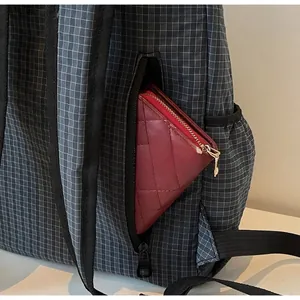 Detail view of the side zipper pocket on a grey plaid backpack with a red wallet inside
