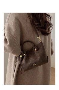 Détail du sac seau en cuir marron foncé avec boucles dorées sur fond de manteau