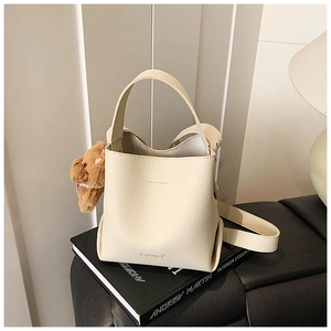 Detail of cream bucket bag with litchi texture, plush bear charm and adjustable strap