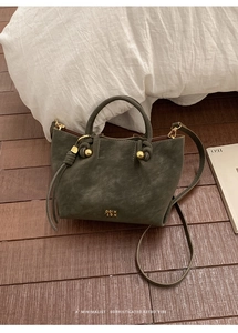 Gros plan sur le sac seau en cuir mat vert foncé avec logo doré et poignée ronde
