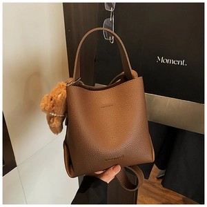 Close-up of brown litchi grain leather bucket bag with plush bear charm and pearl chain