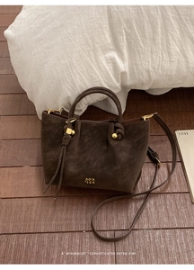 Détail d'un sac seau rétro en daim marron foncé avec logo doré et pompon élégant