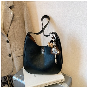 Detail of black hobo bag with silver twist lock and decorative heart charm on a suitcase