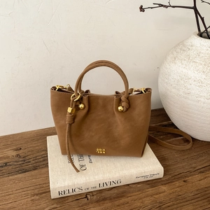 Détail du sac seau marron avec nœud tressé et logo métallique raffiné