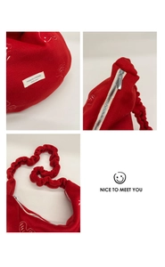 Detail of red plush shoulder bag featuring white floral embroidery and ruched strap
