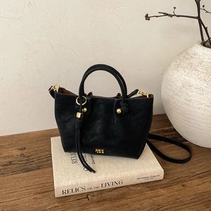 Détail du sac seau en cuir noir avec plis élégants et logo doré sur livres anciens