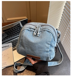 Dettaglio borsa a tracolla in denim azzurro con doppia zip e patch logo in pelle