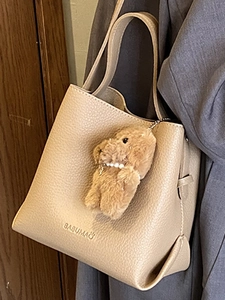 Fashionable beige bucket bag with lychee texture and cute bear pendant on grey suit